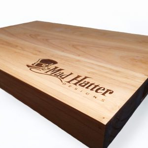 Wooden cutting board with Mad hatter logo engraved on it in the bottom right corner