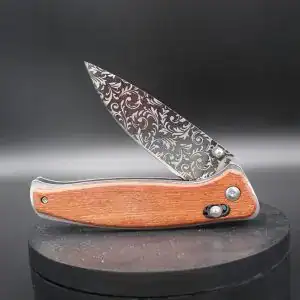 pocket knife flipped open with a floral design engraved in black on the blade